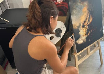 Woman painting a sailboat on canvas in art studio.