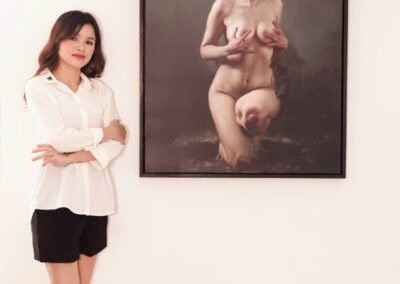 Woman standing next to a large modern art painting of a nude woman with a flower crown.