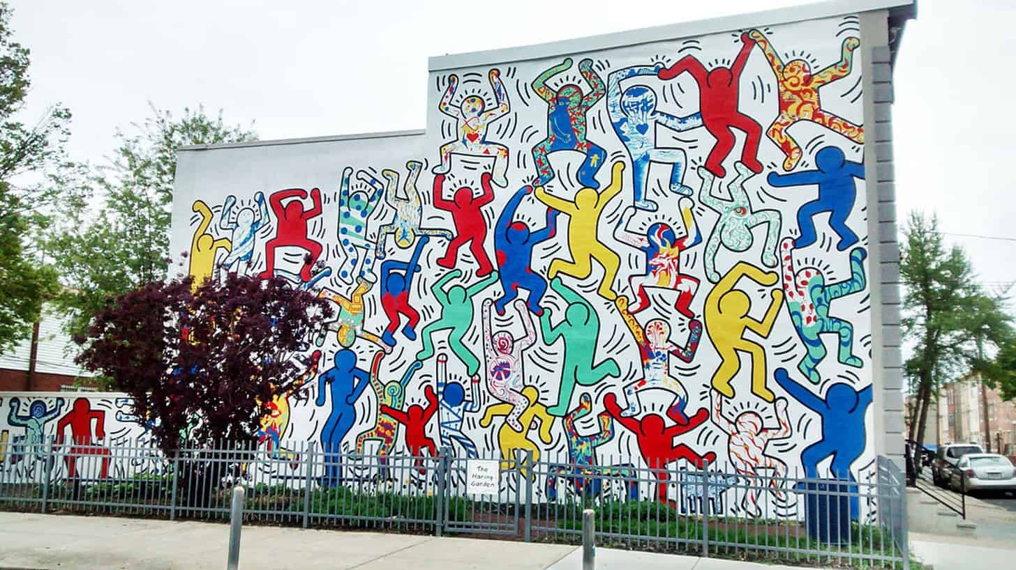 A vibrant artwork depicting Keith Haring's iconic dancing figures, illustrating energy, unity, and universal humanity. In the foreground, a series of stylized, abstract figures, each animated in dynamic poses, showcasing their interconnectedness through bold lines and bright colors like red, yellow, and blue. In the middle ground, subtle outlines of additional figures can be seen, creating a sense of depth and movement. The background features a lively urban setting with soft pastel colors, suggesting a harmonious environment. The lighting is bright and cheerful, enhancing the uplifting mood of the piece, and the angle is slightly elevated to capture the full vibrancy of the dance. The brand "Poppins Shop" subtly integrates with the overall theme, emphasizing creativity and expression.
